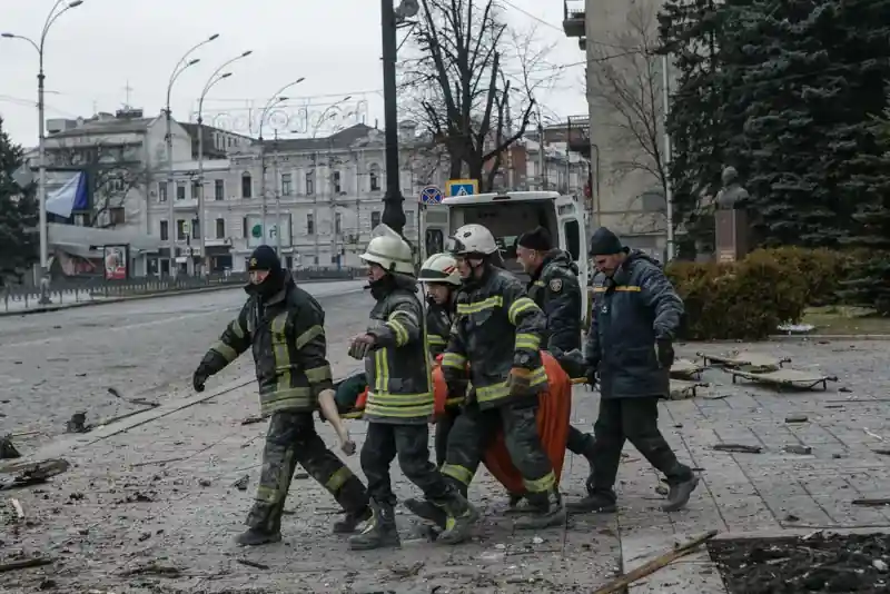 Firefighters carrying a person on a stretcher away from a destroyed building